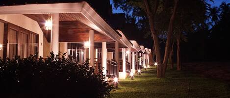 A row of hotel rooms with a covered outdoor area, columns, and a well-lit pathway.