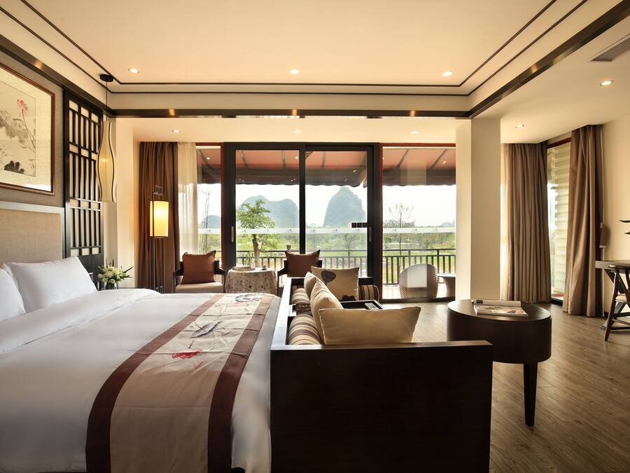 Ein Hotelzimmer mit einem großen Bett, einer Couch, einem kleinen Tisch und einem Balkon mit Bergblick.