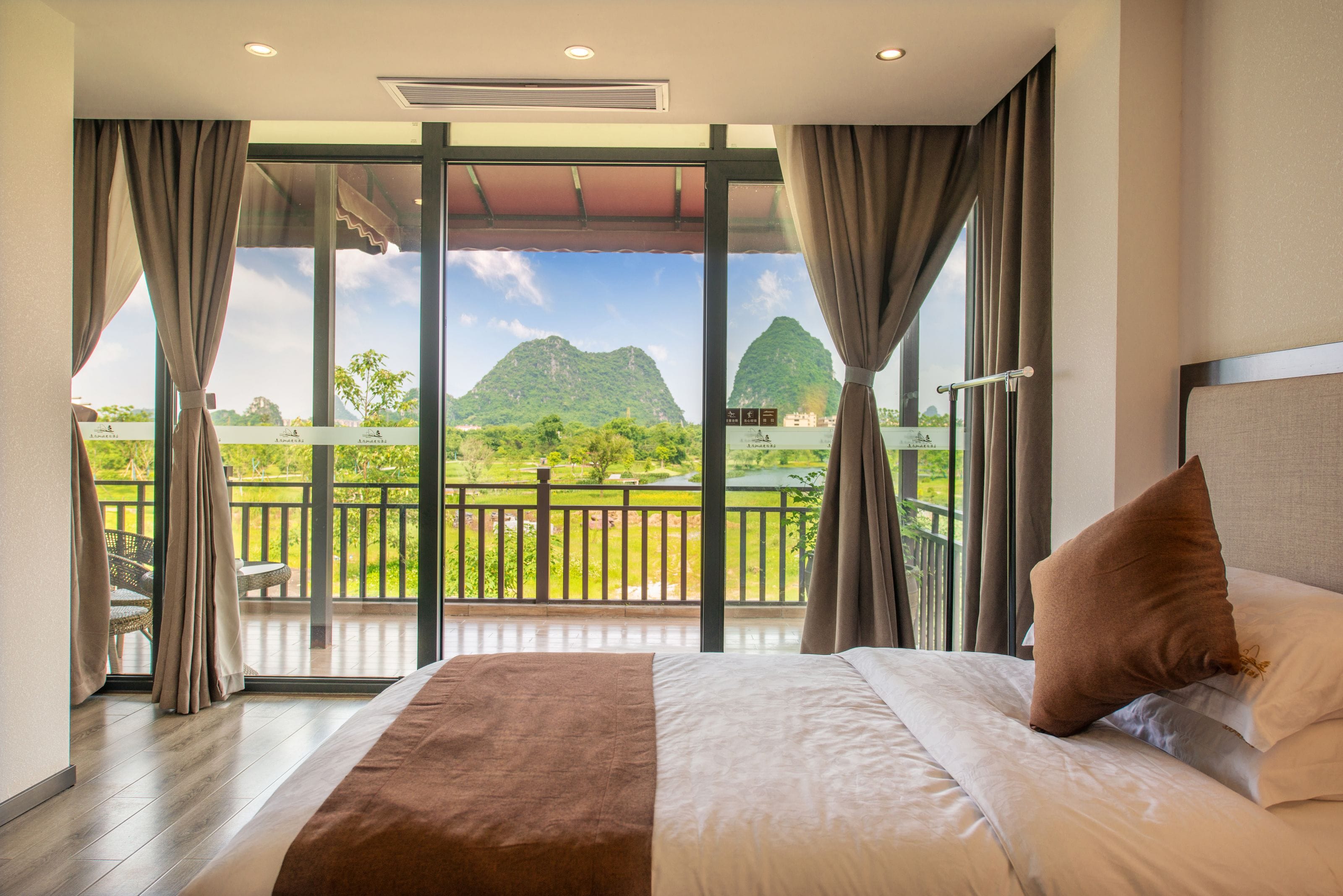 A bedroom with a large bed, a view of a balcony, and a mountain in the background.