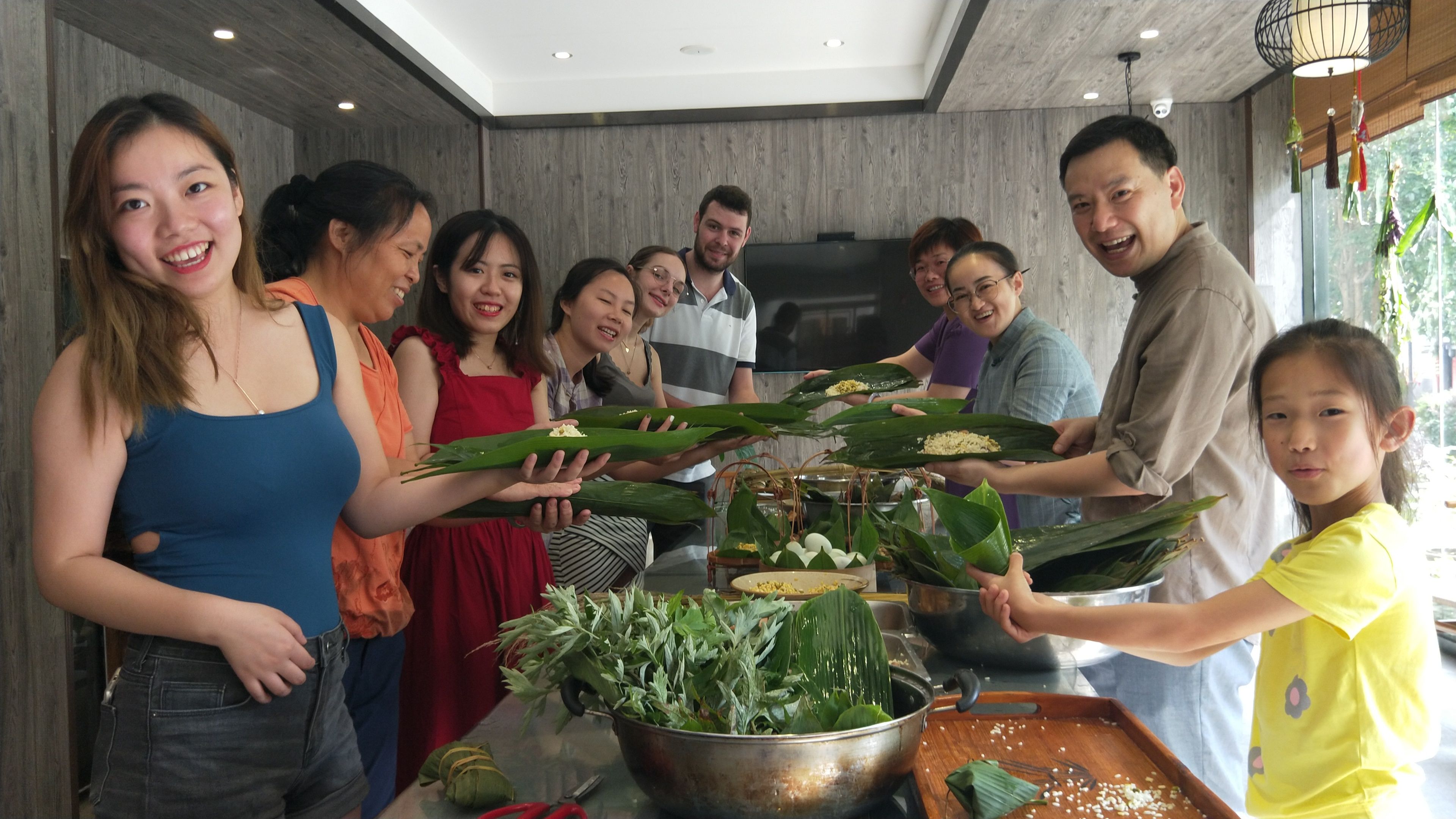 A group of people preparing food with leaves in a modern kitchen with wooden walls and a large window.
