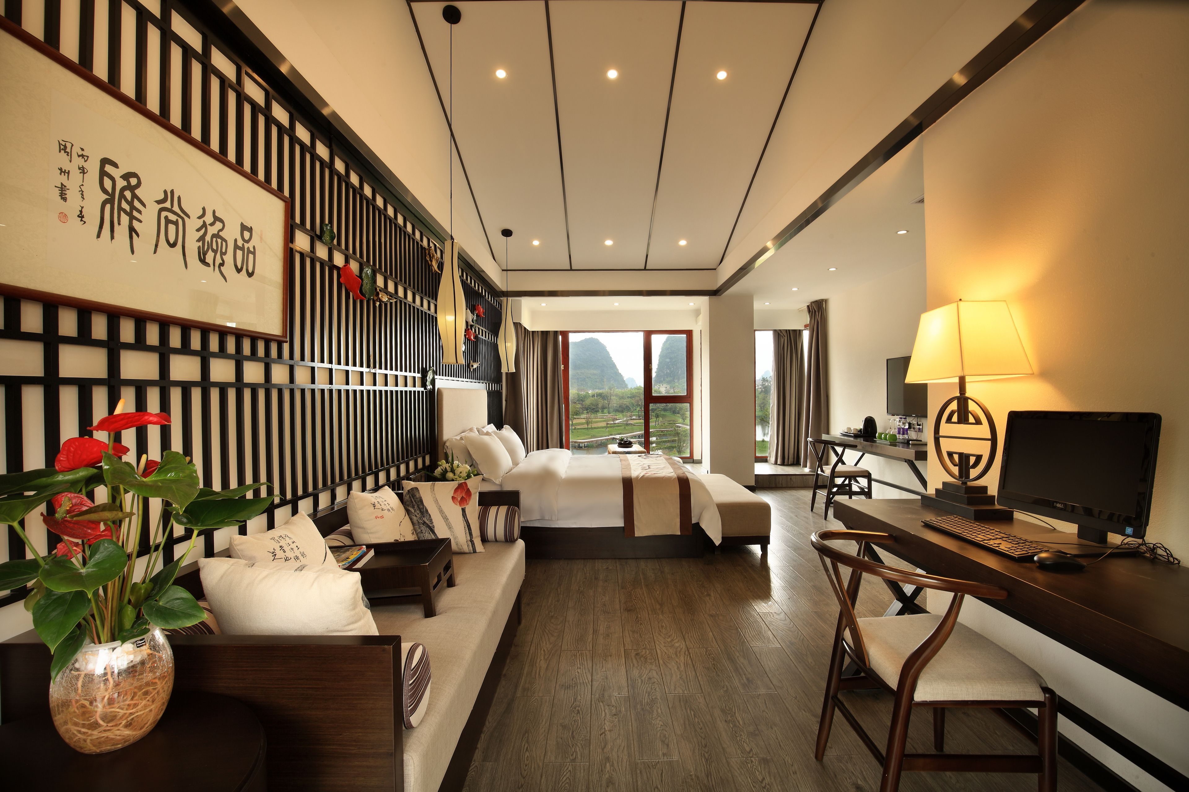 A modern hotel room with a bed, desk, and computer. There is a large window with a view of mountains.