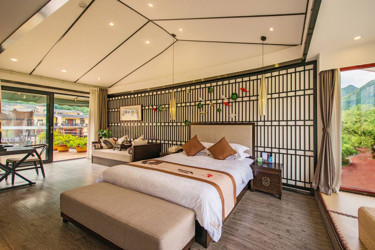 Quarto de hotel moderno com uma cama grande, uma escrivaninha e vista para área verde.