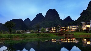 Vista lacustre de un hotel moderno con varias construcciones, un reflejo en el agua y montañas al fondo.