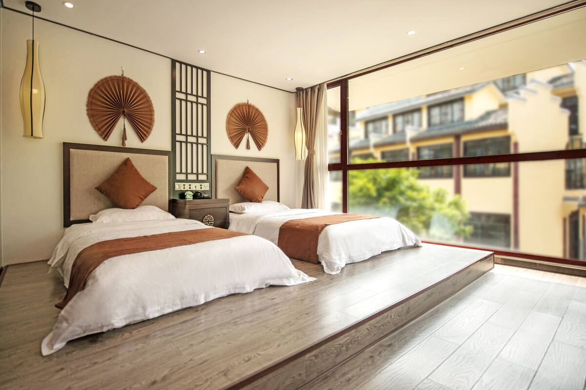 Quarto de hotel moderno com duas camas, uma janela grande e arte decorativa nas paredes.