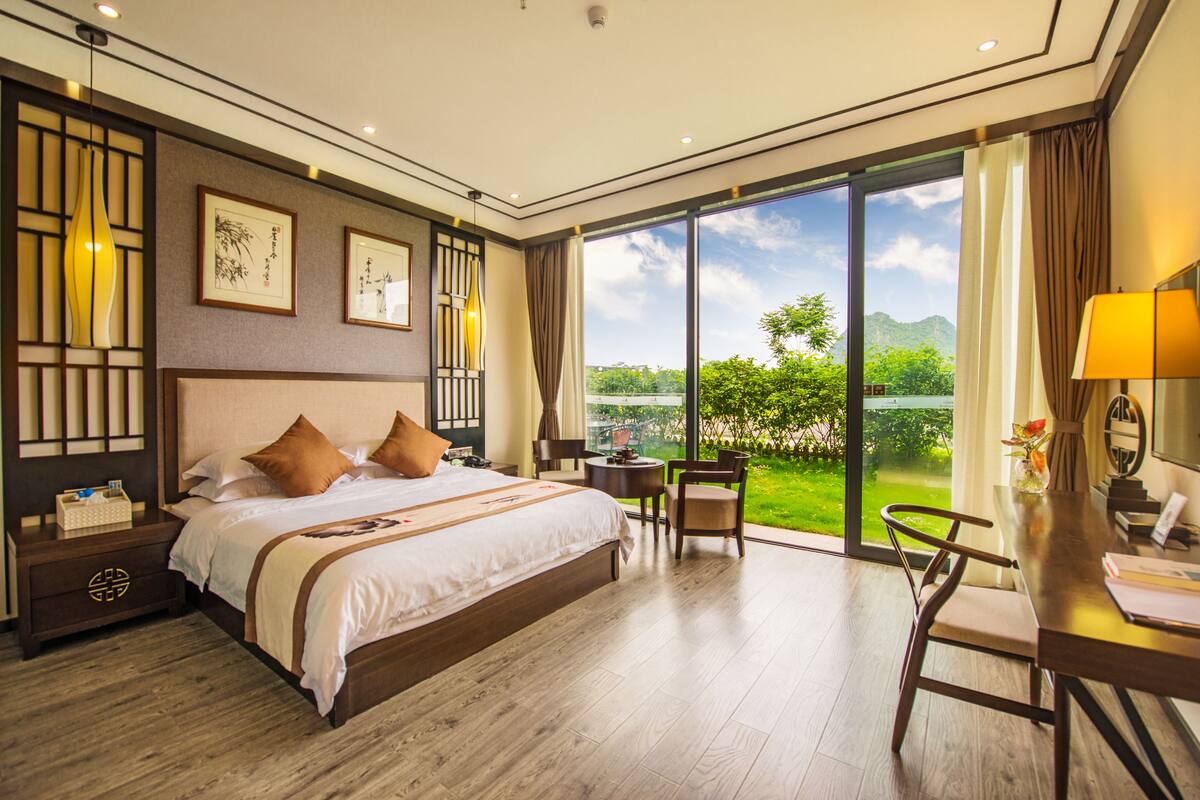 Quarto de hotel espaçoso com uma cama grande, uma mesa de trabalho e vista para um jardim exuberante.
