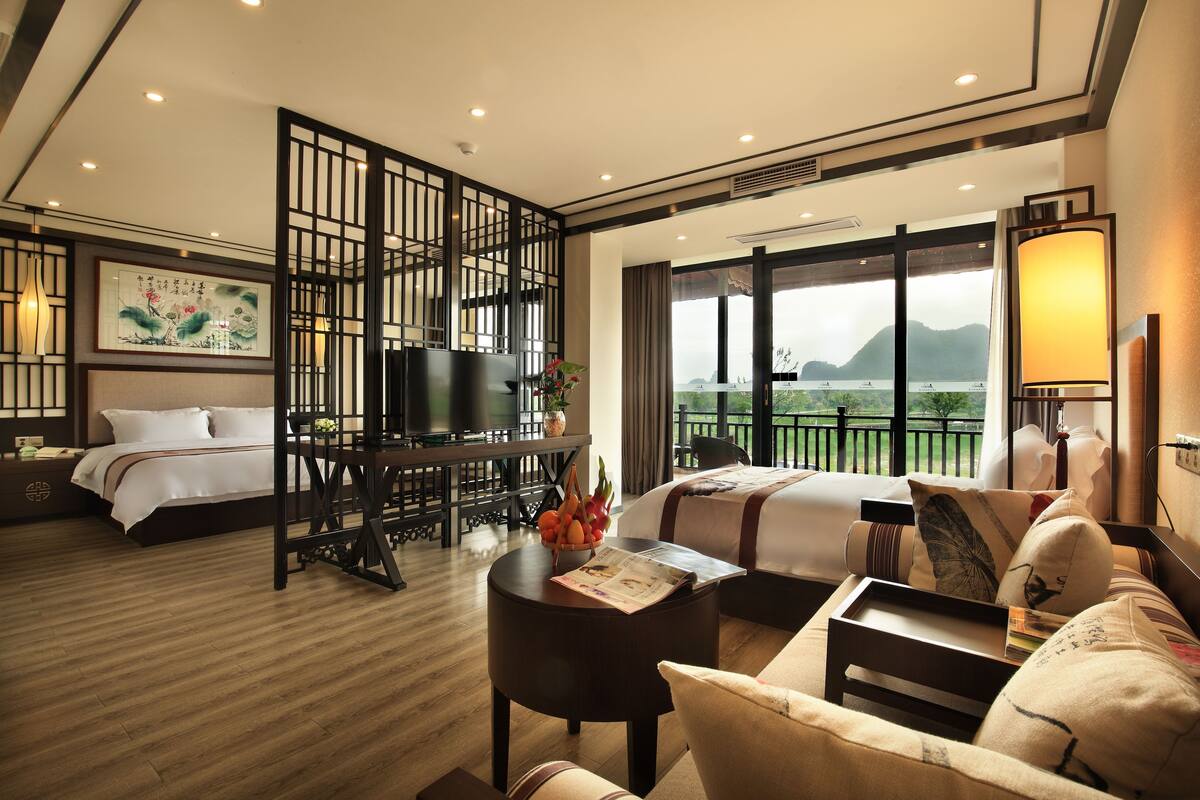 Quarto de hotel com cama, escrivaninha, sofá, televisão e varanda com vista para as montanhas.