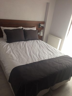 A neatly made bed with white and dark bedding, a wooden headboard, and a bedside lamp. - Bektas Karagol Otel (Dereli)