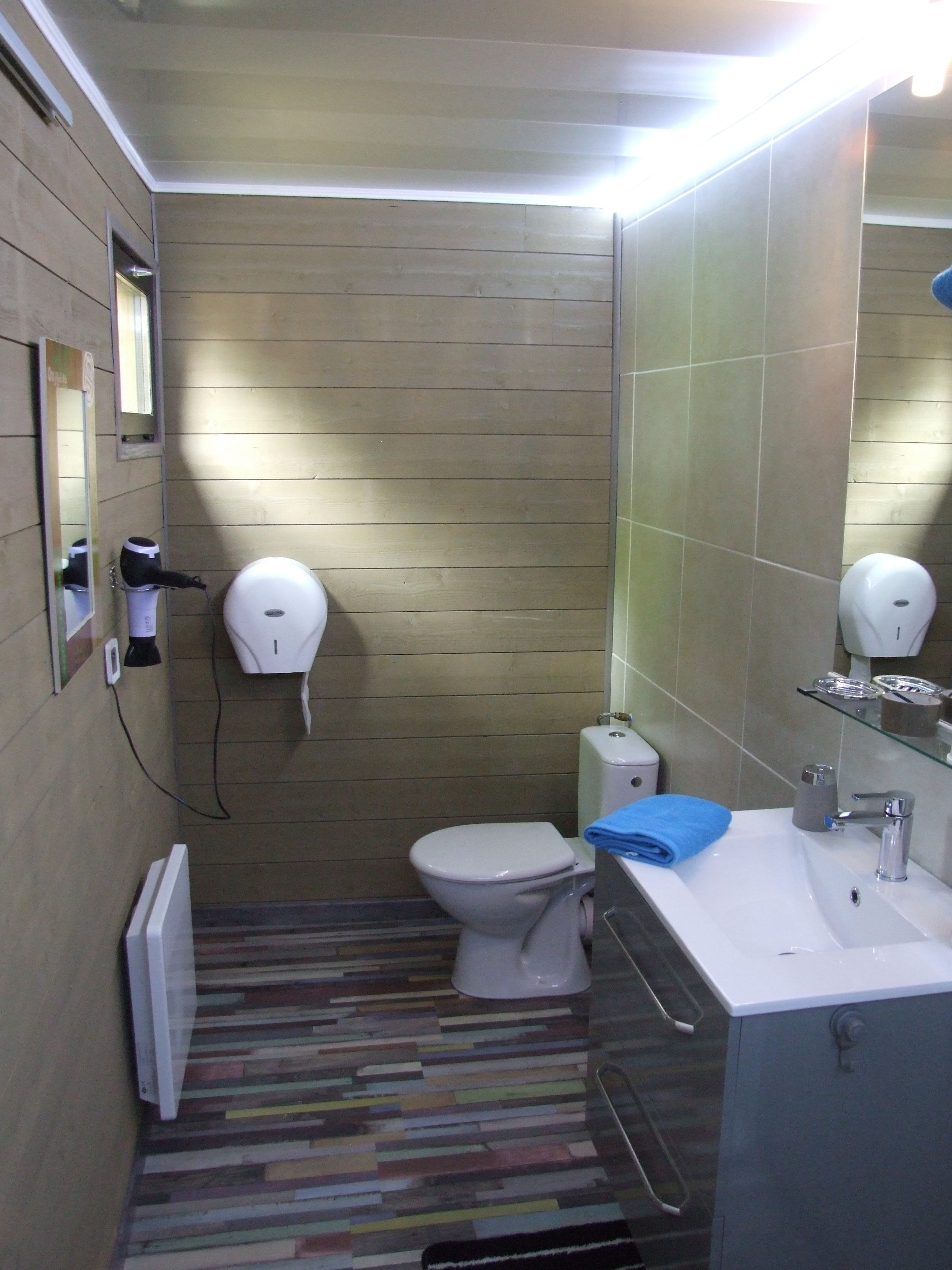 Un bagno piccolo con un water, un lavandino e uno specchio. Si vede un porta asciugamani e un asciugamani ad aria sulla parete.