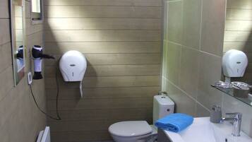 Un bagno piccolo con un water, un lavandino e uno specchio. Si vede un porta asciugamani e un asciugamani ad aria sulla parete.