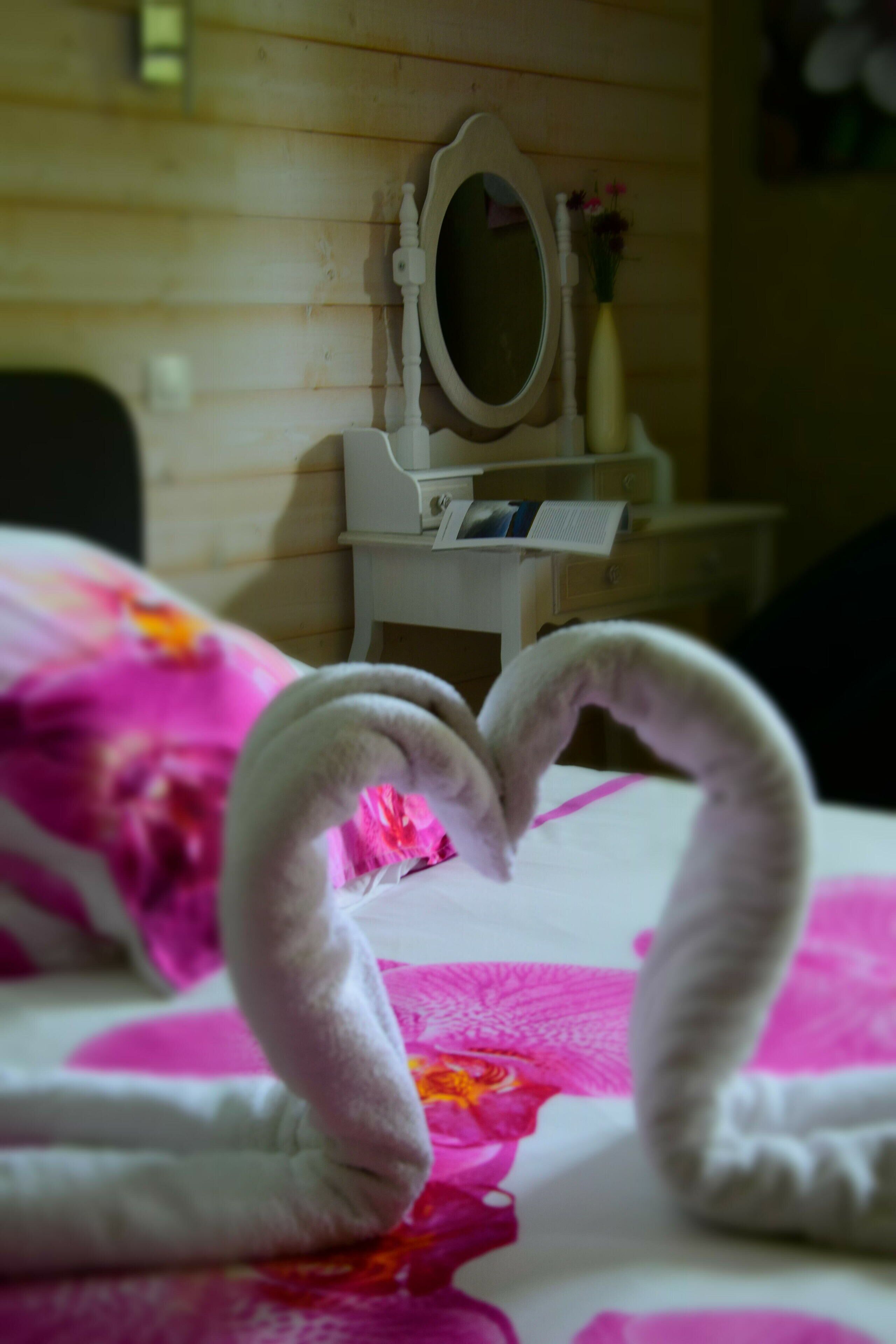Una cama con una toalla dispuesta en forma de corazón y una pared de madera con un espejo y una mesita con un jarrón.