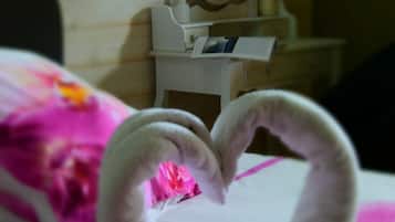 Una cama con una toalla dispuesta en forma de corazón y una pared de madera con un espejo y una mesita con un jarrón.