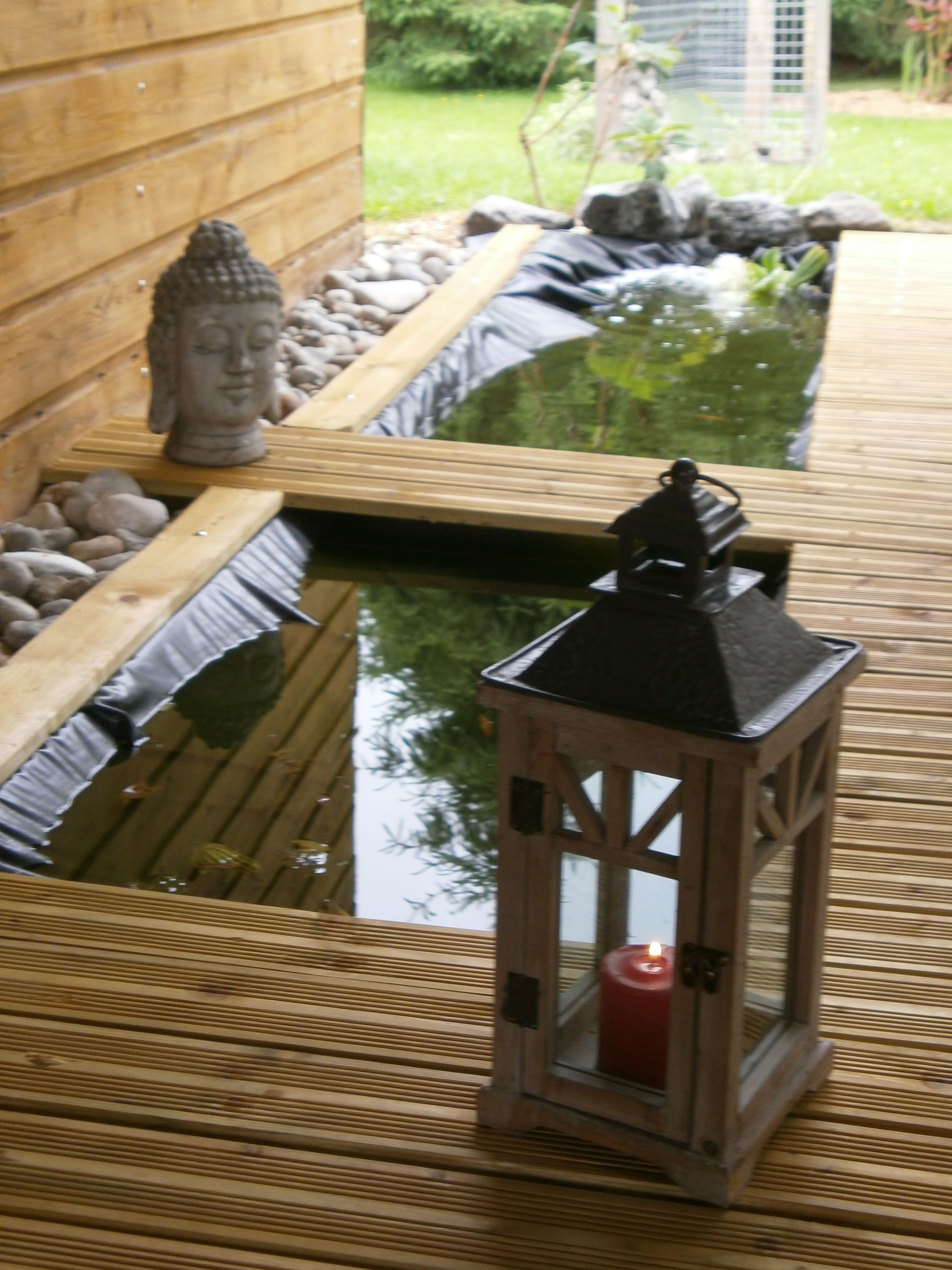 A wooden deck with a small pond, a Buddha statue, and a lantern.