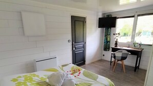 A bedroom with a bed, a desk, a chair, a door, and a window. - Le Clos du Clocher (Gueudecourt)