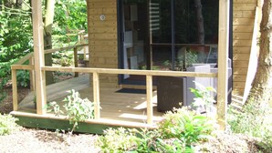 A wooden cabin with a wooden deck, a glass door, and a small outdoor seating area. - Le Clos du Clocher (Gueudecourt)