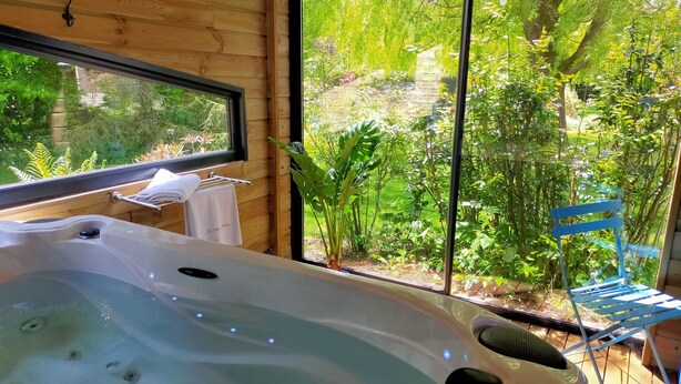 A bathroom with a wooden interior, a bathtub, and a window overlooking a garden. - Le Clos du Clocher (Gueudecourt)