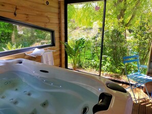 Un baño con detalles de madera, una bañera y un ventanal con vistas a un jardín.