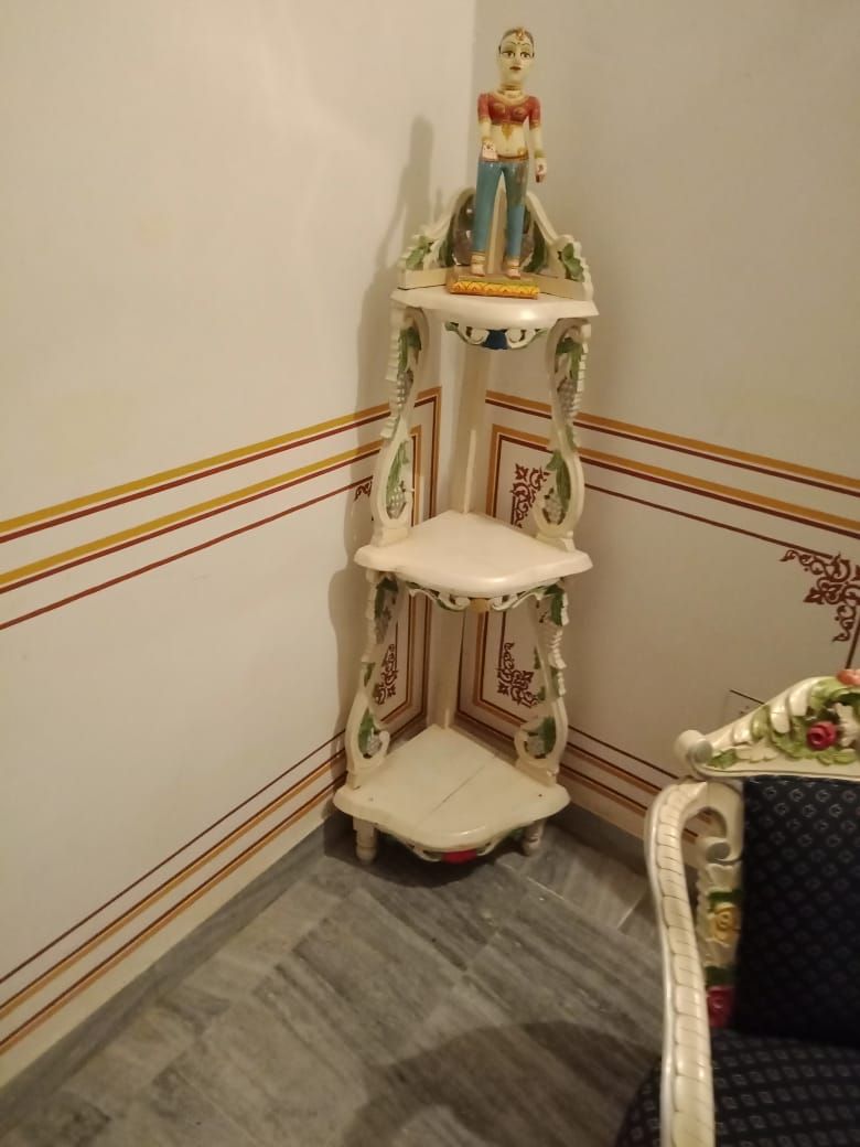 A corner with a decorative white shelf unit with a figurine on top, a patterned wall, and a patterned floor.