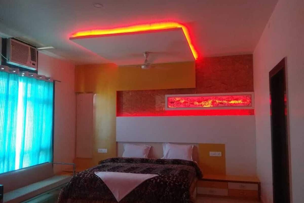 Une chambre à coucher avec un lit, un ventilateur de plafond, une bande lumineuse néon rouge et une fenêtre avec des rideaux.