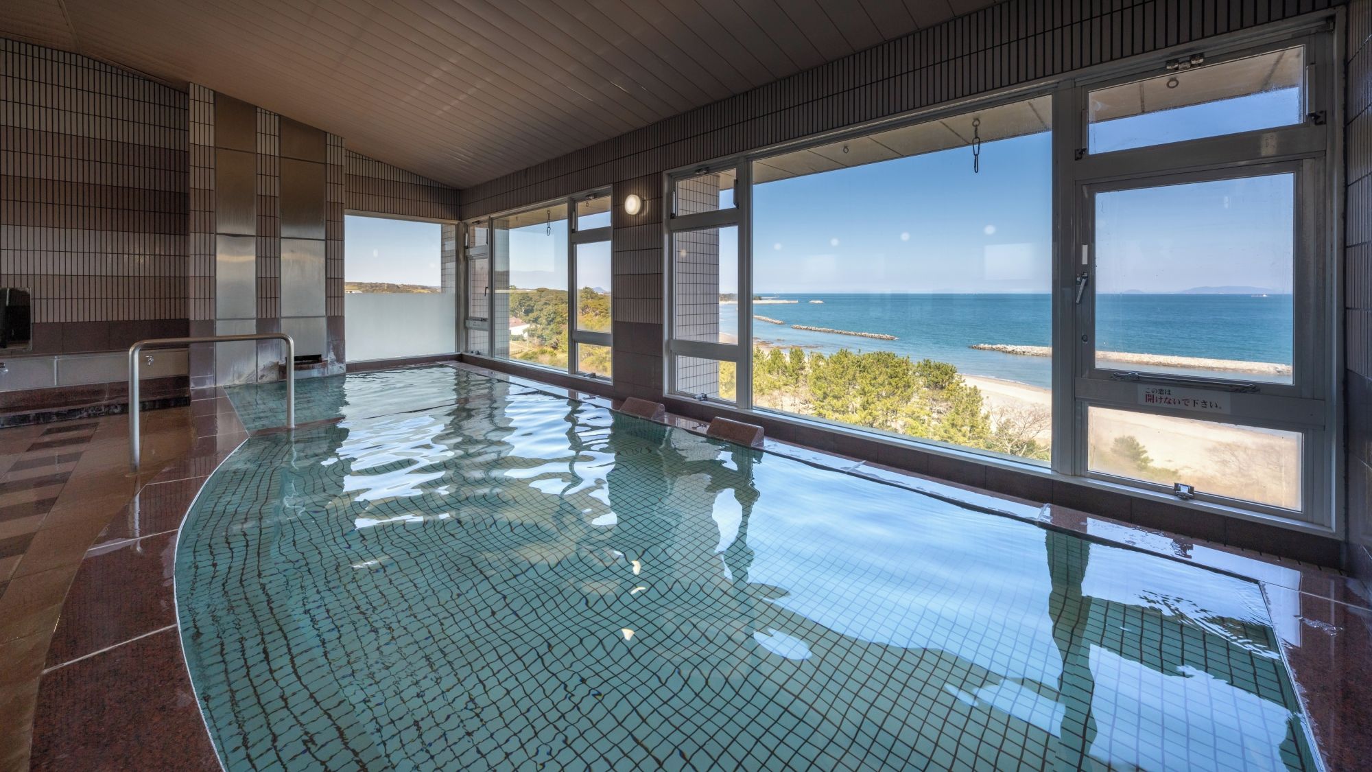 An indoor swimming pool with a view of the sea and beach.