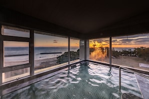 An indoor swimming pool with large windows offering a view of the sunset over the ocean. - Villa Kunisaki (Kunisaki)
