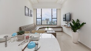 A modern dining area with a large window, a sofa, and a television on the wall. - Macy Studio Apartment (Ho Chi Minh City)