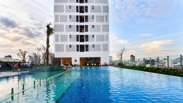 A modern building with a rooftop pool, surrounded by greenery and a cityscape in the background. - Macy Studio Apartment (Ho Chi Minh City)