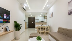 A modern living room with a flat-screen TV, a coffee table, a sofa, and a dining area with a table and chairs. - Macy Studio Apartment (Ho Chi Minh City)