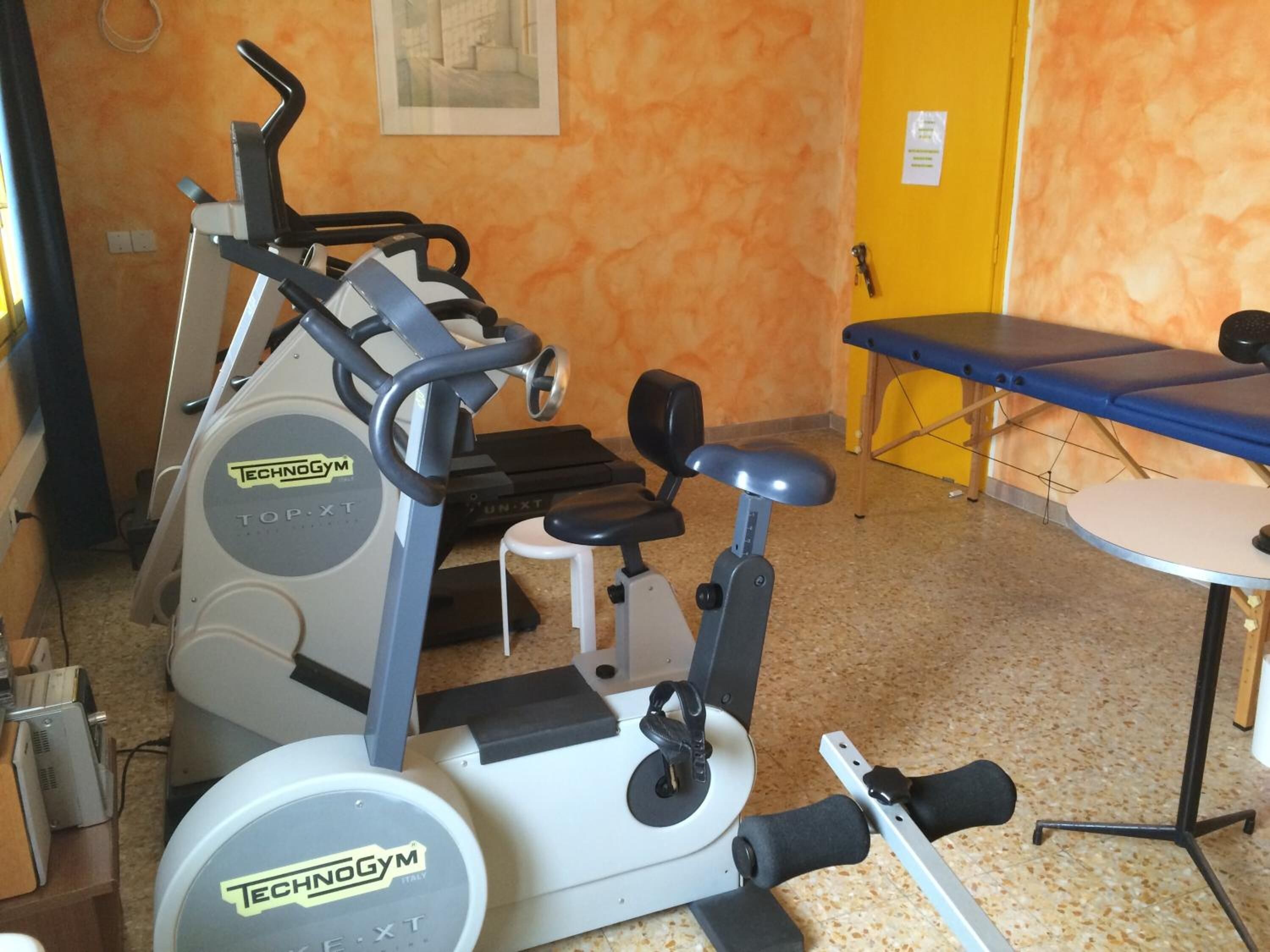 A gym with a stationary bike, a bench, and a small table.