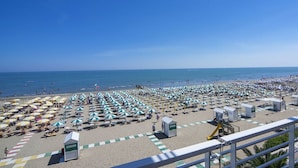 A beach with rows of umbrellas and beach chairs, a clear sky, and the ocean in the background. - Hotel Ariston (Caorle)