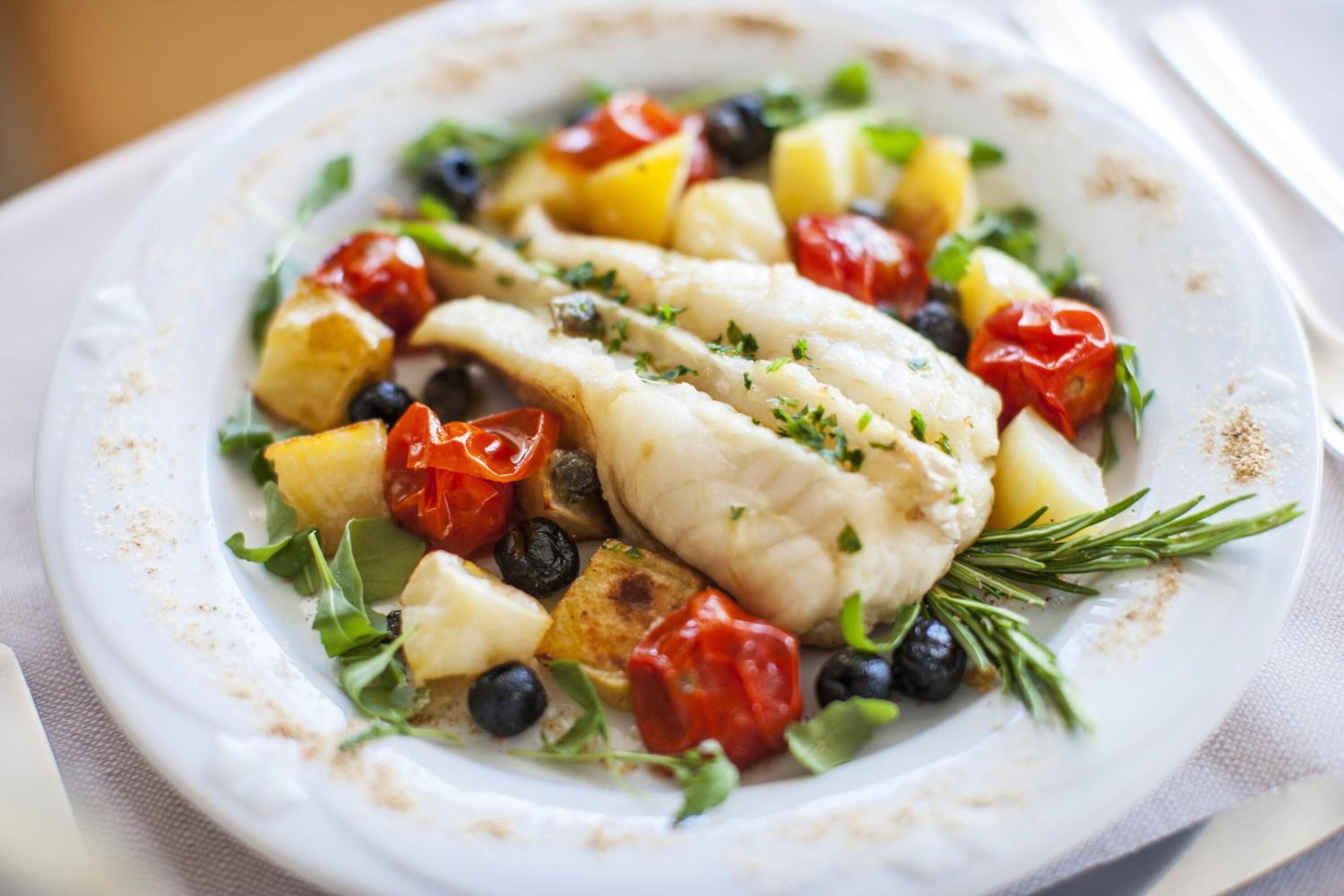 A plate of fish with vegetables and herbs.