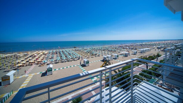 A beach view from a balcony with umbrellas, beach huts, and a clear blue sky. - Hotel Ariston (Caorle)