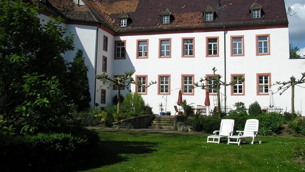 A large white building with red window frames and a sloped roof. - Schloss Triestewitz (Arzberg)