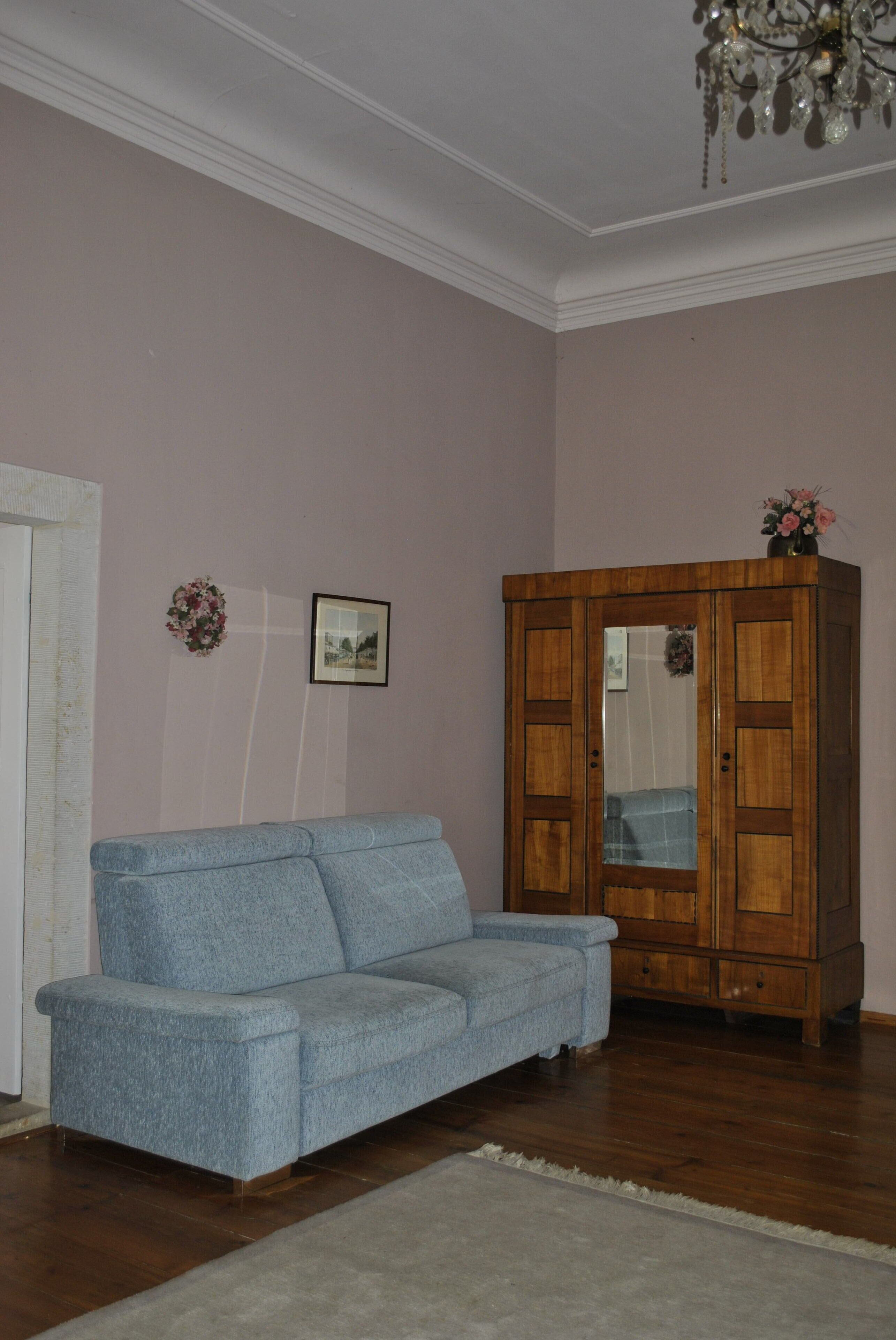 A room with a blue sofa, wooden cabinet, and a chandelier.
