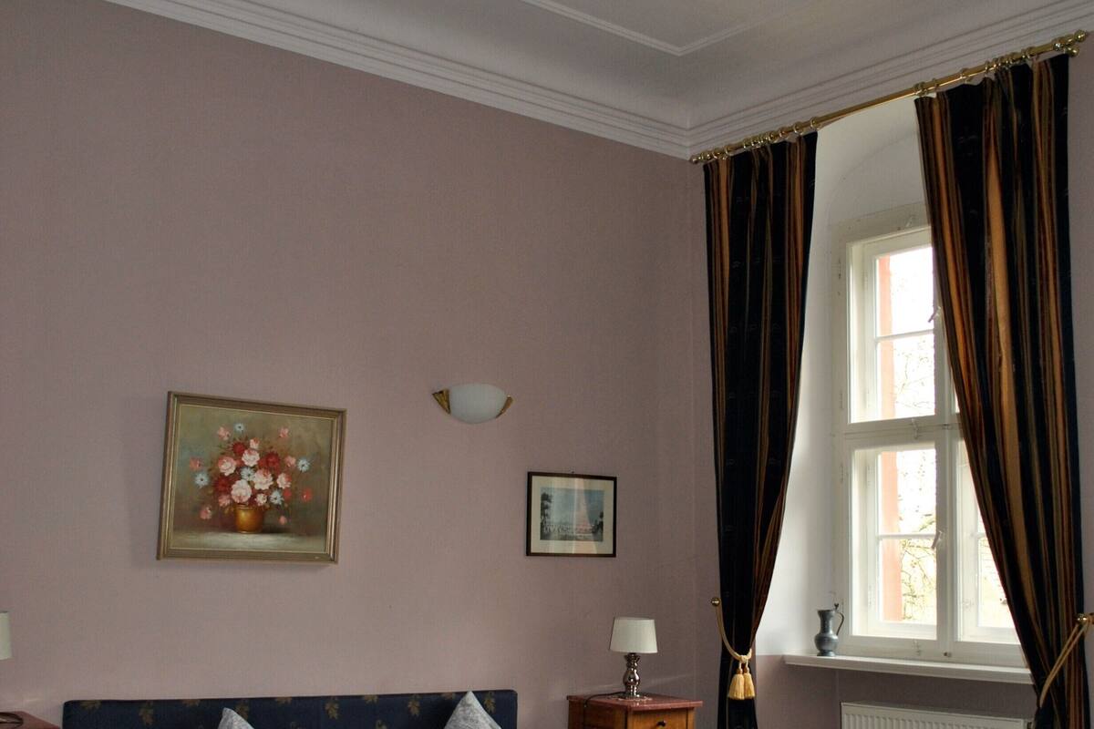 A bedroom with two beds, a chandelier, a window with curtains, and a painting on the wall.