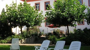 A white building with a red roof, surrounded by green trees and a lawn with white lounge chairs. - Schloss Triestewitz (Arzberg)