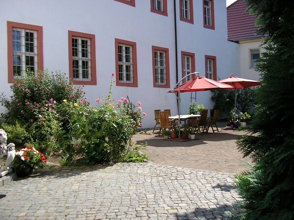 A courtyard with a cobblestone path, a table with chairs, and a red umbrella.