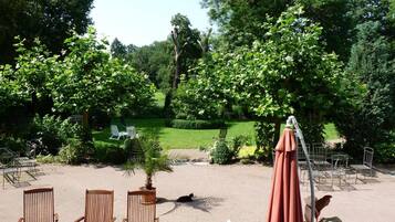 An outdoor patio area with a round wooden table and chairs, surrounded by greenery and trees.