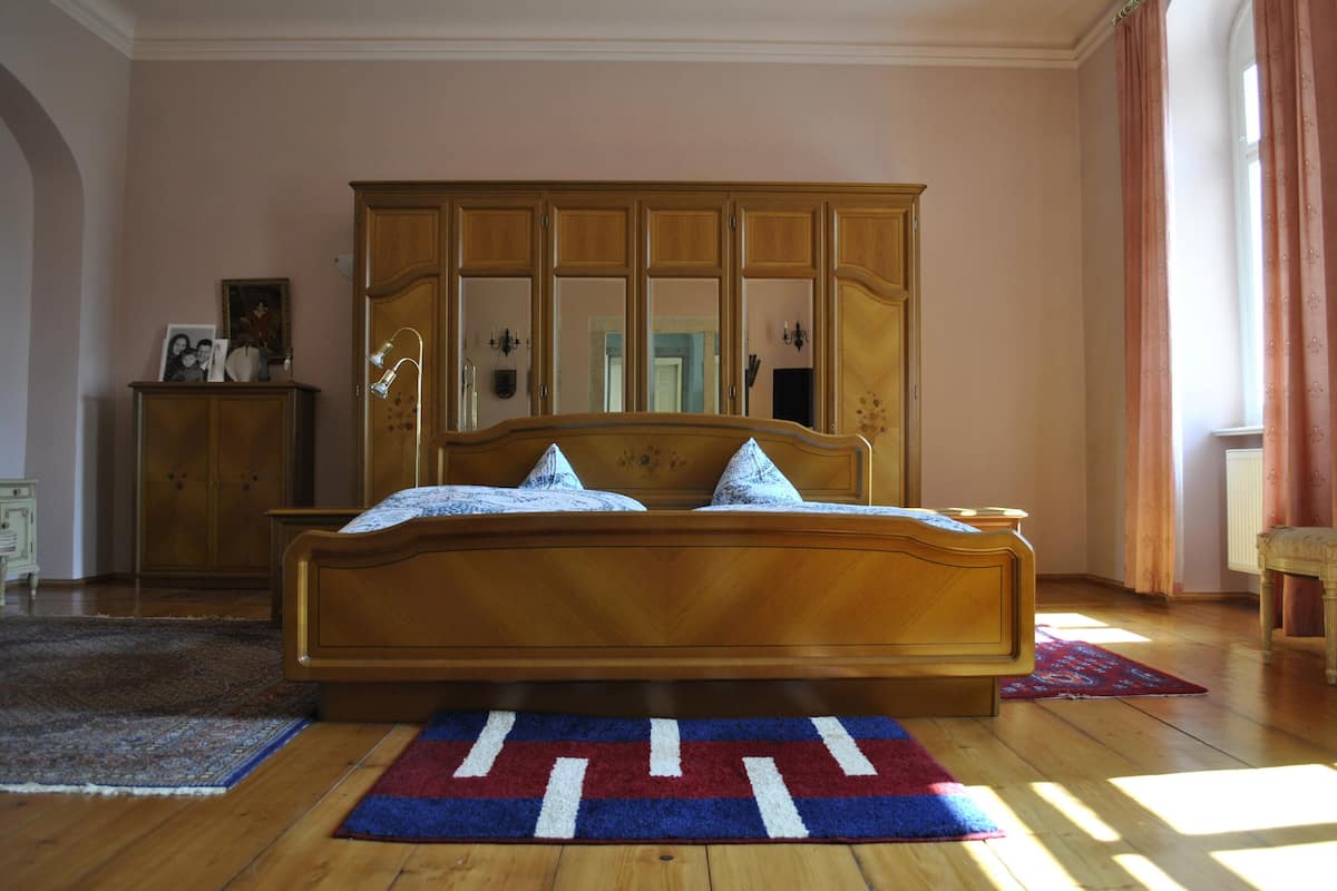 A bedroom with a wooden bed, a large mirror above the bed, and a wooden wardrobe.