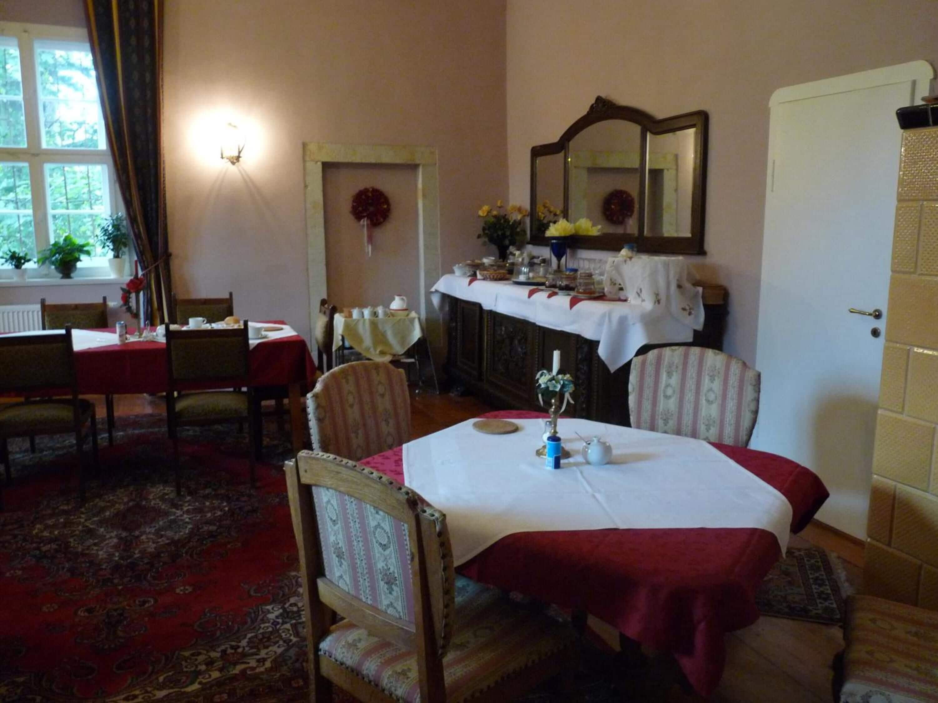 Une salle à manger avec une table dressée pour quatre personnes, un miroir au-dessus de la table et une porte sur la droite.