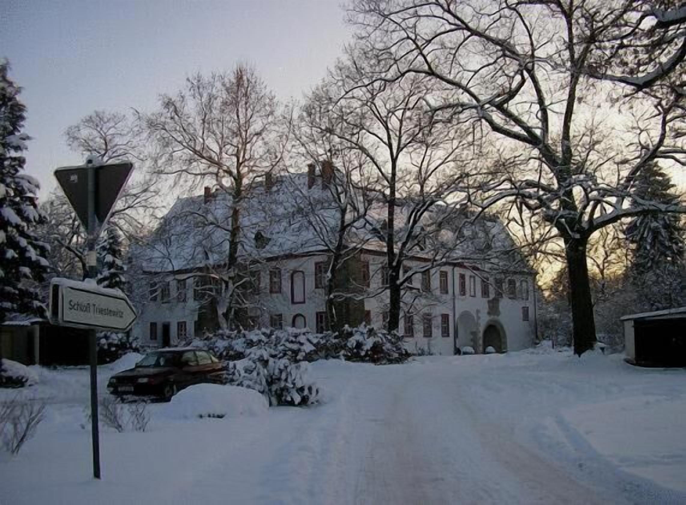 Un carrer cobert de neu amb un edifici gran i històric, amb nombroses finestres i una entrada destacada.