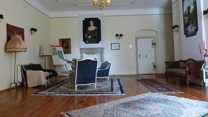A spacious room with hardwood flooring, a fireplace, and a large rug. There are two chairs and a table with a lamp. - Schloss Triestewitz (Arzberg)