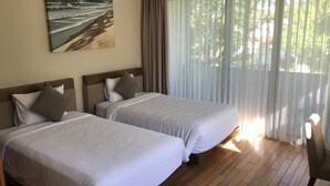 Hotellihuone, jossa on kaksi sänkyä, taulu seinällä ja näkymä vehreään maisemaan läpikuultavien verhojen läpi.