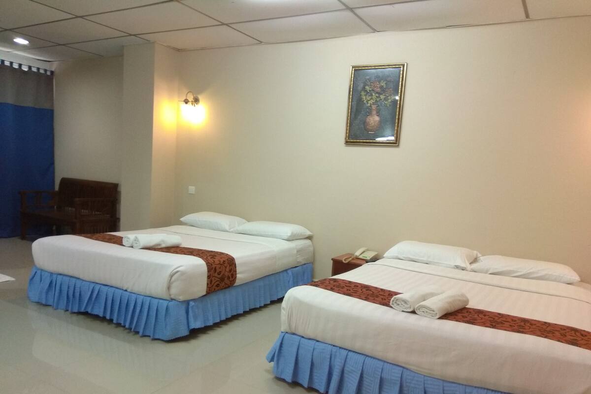 A hotel room with two beds, each with white linens and blue skirts. There is a painting on the wall and a telephone on the nightstand.
