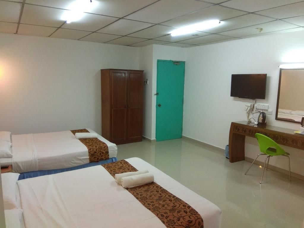 A hotel room with two beds, a desk with a chair, a television, and a green door.
