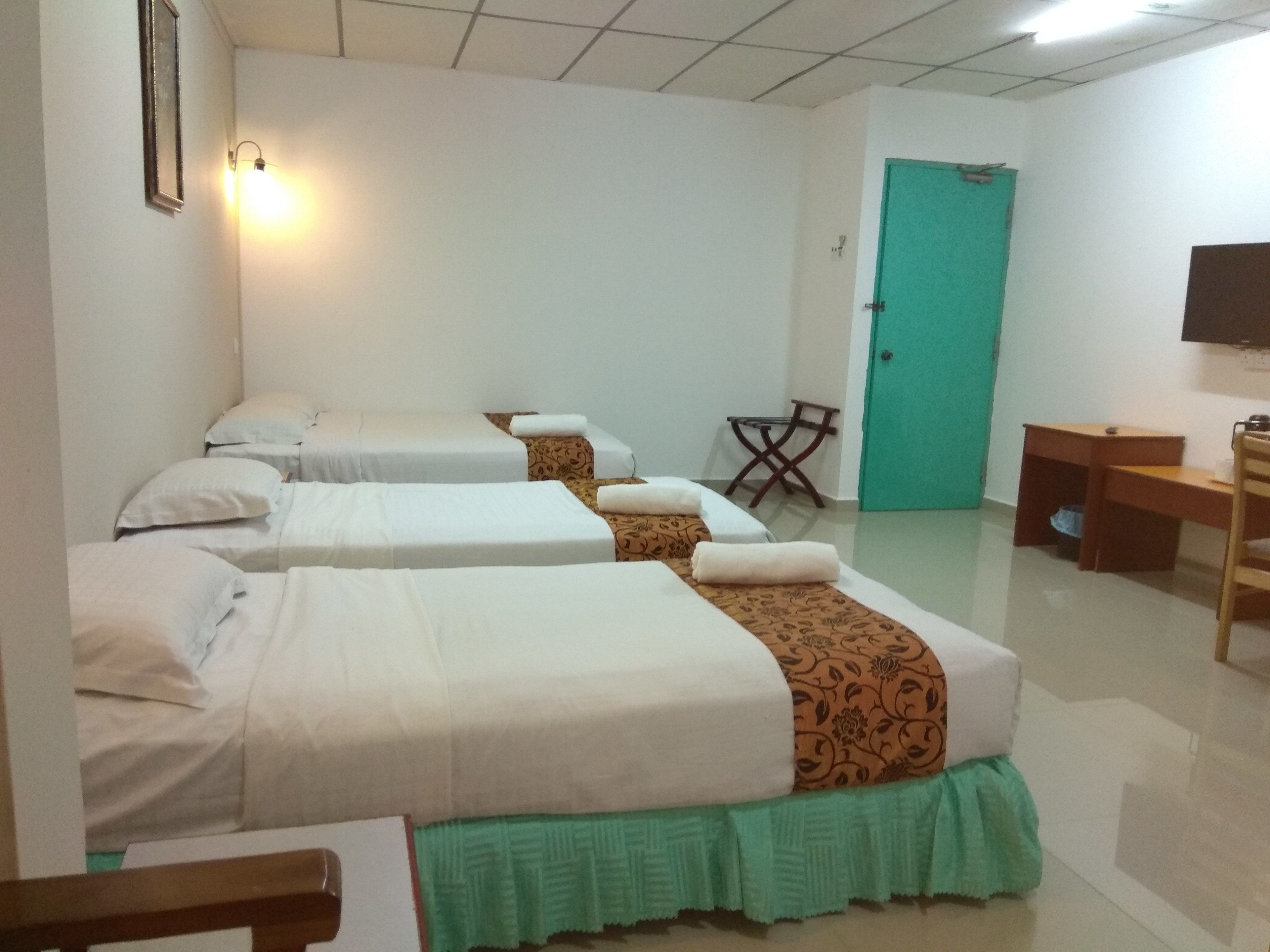 A hotel room with three beds, a desk, a chair, and a television on the wall.