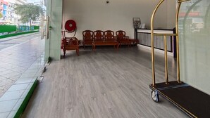 Een hotel lobby met een receptiebalie, verschillende houten stoelen, een brandslanghaspel en een trolley.