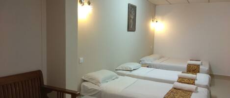 A hotel room with three single beds, a wooden bench, and a small table.
