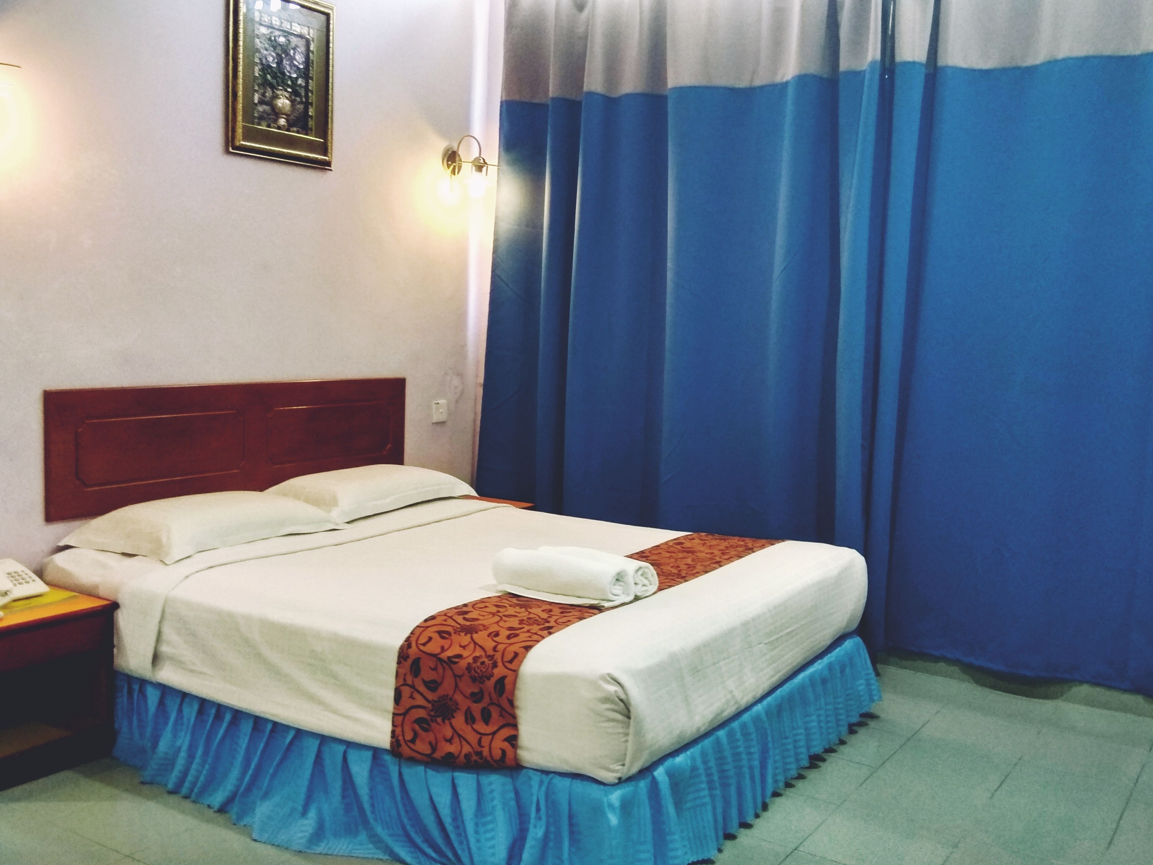 A hotel room with a bed, a nightstand, a telephone, and a wall-mounted light fixture.