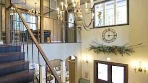 A multi-level interior with wooden stairs, a chandelier, a ceiling fan, and a wall-mounted clock. - Chambre d'hôte  Étoile et fées (Komatsu)