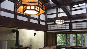 A traditional interior with a wooden table, chairs, a fireplace, and large windows. - Chambre d'hôte  Étoile et fées (Komatsu)